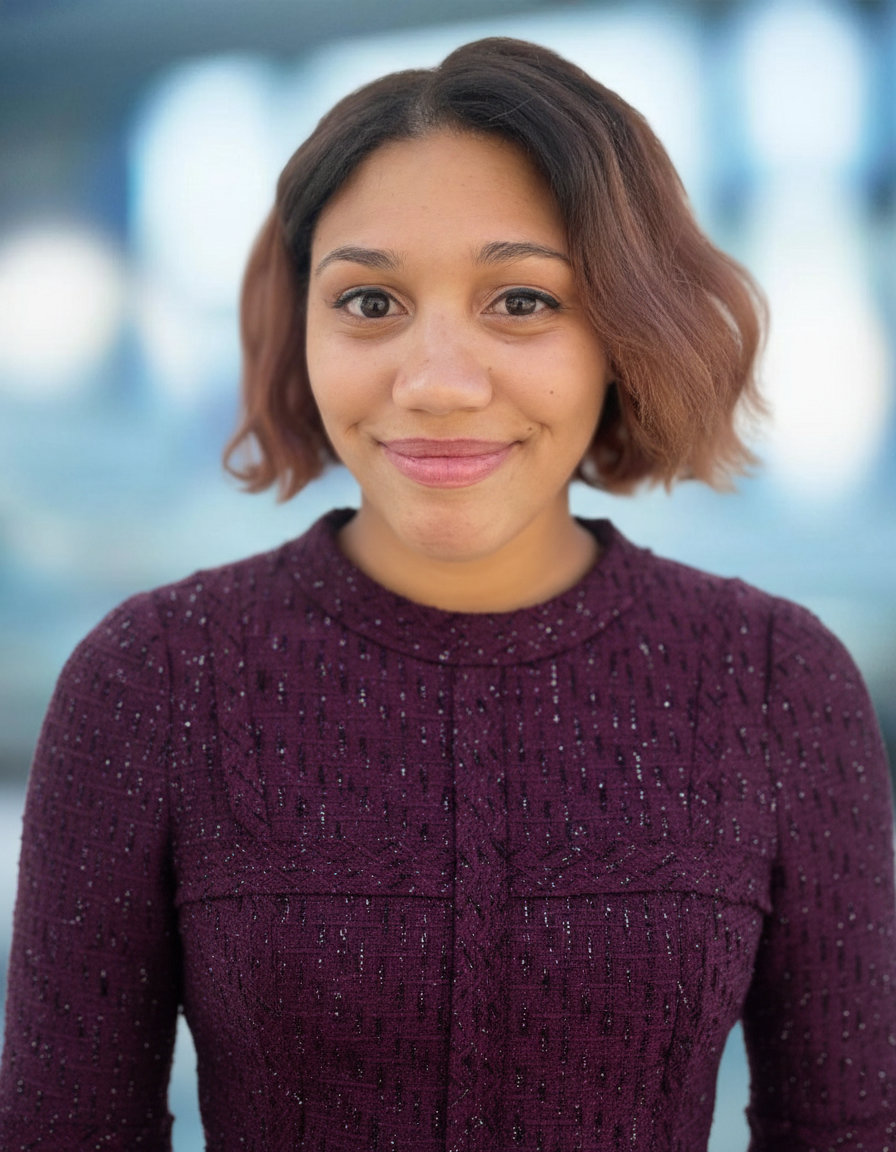 Headshot of Malika wearing a smart business suit, on a rooftop with a city skyline in the background.